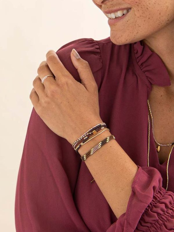 Le modèle porte un bracelet dans les tons rose, or et rouge-violet avec un petit pendentif en or.