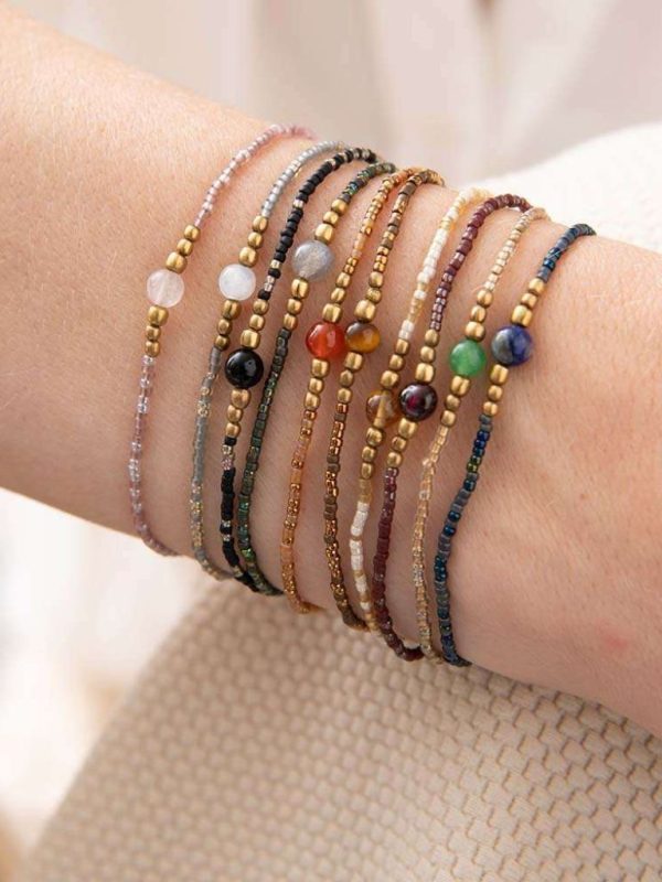 Nahaufnahme von einem Arm, einer Frau, die mehrere Armbänder an hat. Die Armbänder sehen alle gleich aus, sind jedoch alle in verschiedenen Farben resp. sind mit verschiedenen Edelsteine.