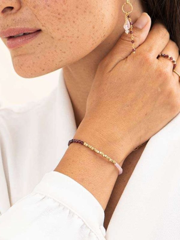 Modell trägt ein Armband mit Gold, Rosa und Roten kleinen Edelsteinen. Das Modell ist nur teilweise ersichtlich. Sie hält sich am Hals, damit das Armband gut ersichtlich ist.